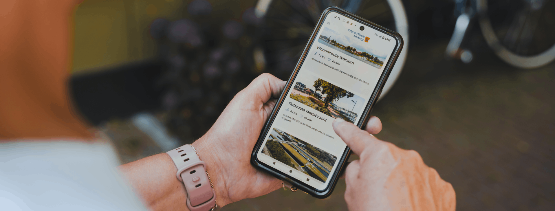 Een vrouw houdt een smartphone vast waarop de Erfgoedroute Limburg App is geopend, waarmee een route van De legende van Sint Joris en de Draak wordt ontdekt