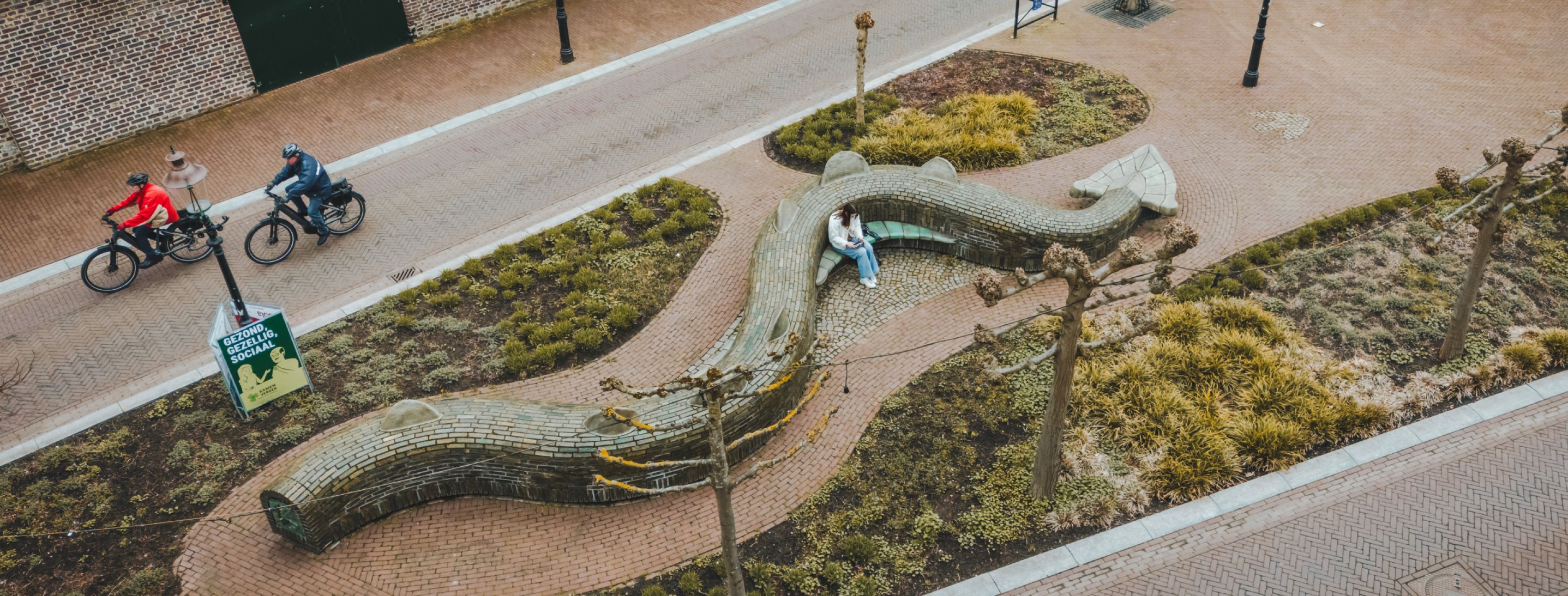 Fietsers langs een kronkelende bank in de vorm van een draak in Beesel, onderdeel van de route die de legende van Sint Joris en de Draak zichtbaar maakt