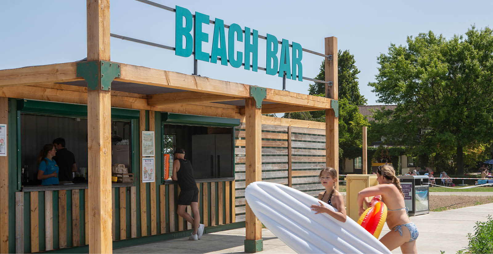 Beach bar met op de voorgrond kinderen met een surfplank