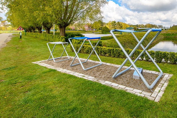 Drie metalen objecten in een grasveld langs het water, onderdeel van de kunst langs de Maasfietsroute.