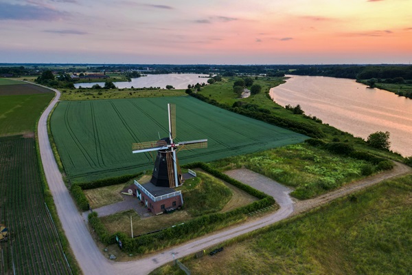 Luchtfoto van molen De Grauwe Beer in Beesel, omringd door akkers en met uitzicht op de Maas bij zonsondergang.