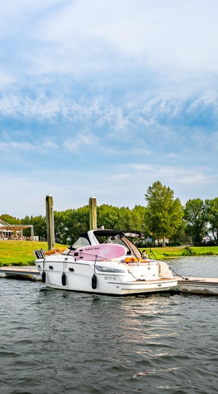 Witte motorboot aangemeerd aan een steiger bij groen landschap en blauwe lucht in Limburg.