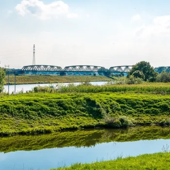 Spoorbrug bij Buggenum over het water, met groen landschap op de voorgrond.