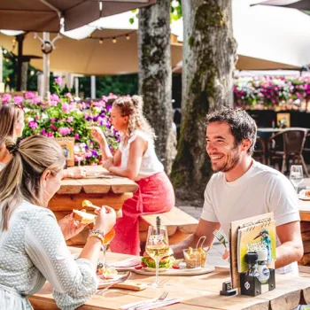 Mensen genieten van eten en drinken op het terras van Boscafé De Busjop, omringd door groen.