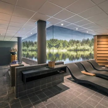 Wellnessruimte met ligstoelen en sauna in Boshotel Vlodrop, met een wandafbeelding van een bos en water.