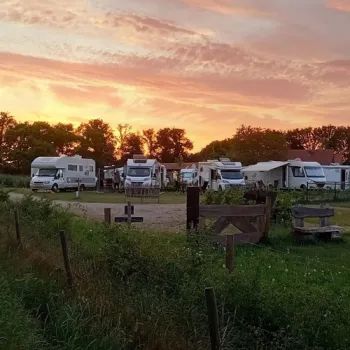 Campers staan op Camperplaats Houbenhof in Leveroy, midden in het groen tijdens een kleurrijke zonsondergang.