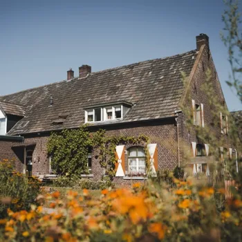 Authentieke Maasdalhoeve van Genaenhof, omringd door bloemen en groen in het Limburgse landschap.