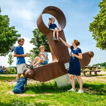 Gezin pauzeert bij het Drakenzwaard in Beesel, een opvallend kunstwerk langs de Maasfietsroute.