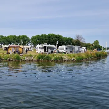 Caravans en campers staan aan de waterkant van Comfortparc Watersportcamping, met uitzicht over de Koeweide Plas.