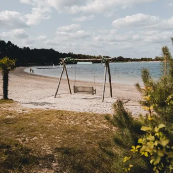 Houten schommel staat op het zandstrand aan de Maasplassen, met uitzicht over het rustige water.