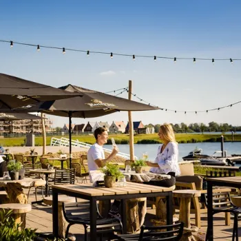 Gasten zitten op het terras van Humphrey’s in Thorn, met uitzicht over de jachthaven en de Maasplassen in de avondzon.