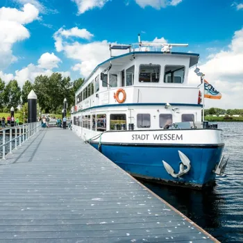 Rondvaartboot Stad Wessem ligt aangemeerd aan de steiger, klaar voor een ontspannen tocht over de Maasplassen.