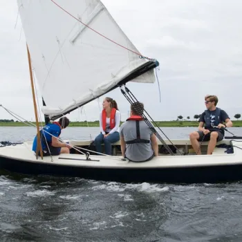 Groep zeilt op de Maasplassen in een open zeilboot, met de wind in de zeilen.