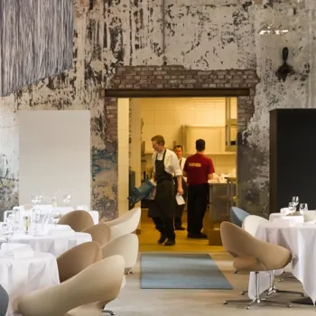 Interieur van Restaurant One in Roermond met gedekte tafels en zicht op de open keuken in een industriële setting.