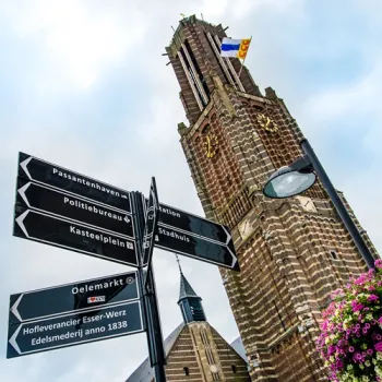 De Martinustoren in Weert steekt boven het centrum uit, met richtingborden op de voorgrond en bloemen langs de straat.