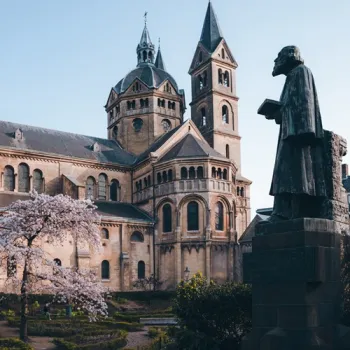 Munsterkerk in Roermond met op de voorgrond het standbeeld van architect Pierre Cuypers, omringd door een tuin met bloeiende bomen.