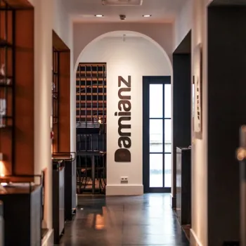 Interieur van Restaurant Damianz in Roermond, met zicht door een booggang naar een stijlvolle ruimte en de naam ‘Damianz’ op de muur.
