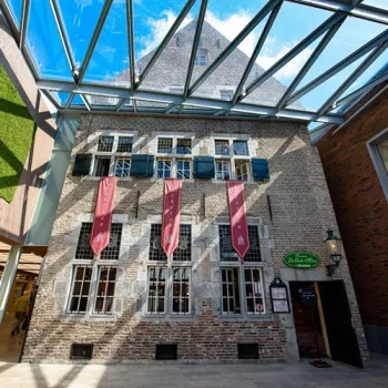 Historisch pand van Taverne de Oude Munt in Weert, met bakstenen gevel, luiken en overkapping in een overdekte passage.