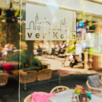 Raam met logo van Brasserie ver’Koch, met uitzicht op het terras op het Munsterplein in Roermond.